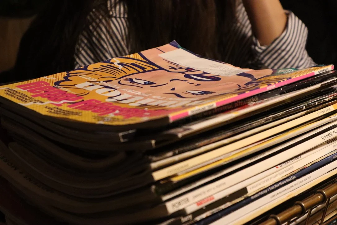 A stack of magazines on a table with one magazine partially open, showing a cartoon character on the cover.